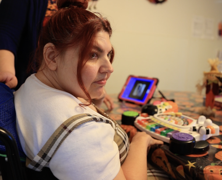 Client at Supportive Concepts for Families sits in her wheelchair alongside an aide during a group Halloween craft activity