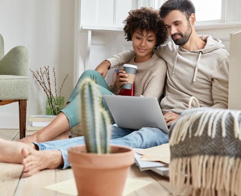 Couple sits together on floor of living room looking at a laptop screen